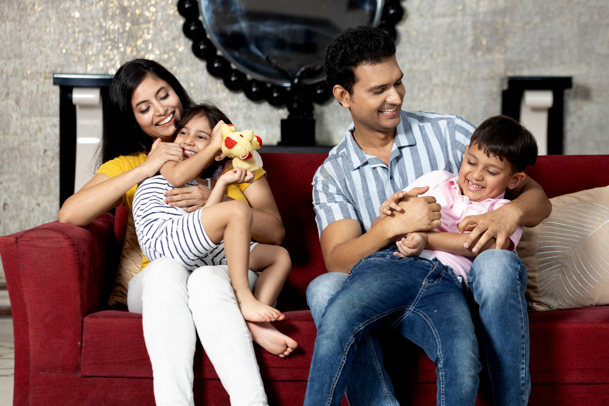 Portrait of Indian family together sitting on sofa in living room looking at each other and having fun.